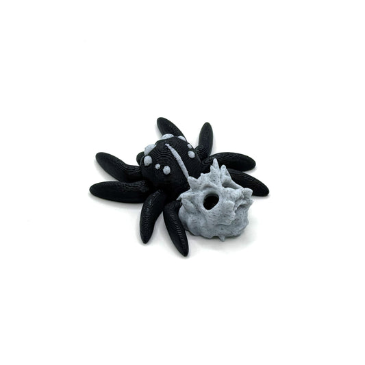 The back view of a black spider with white dots on its back, eight legs, and a hollow gray skull attached, resting on a white surface.