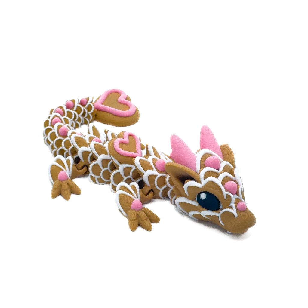 A brown dragon figure with white icing-like patterns, pink hearts, and blue eyes, lying on a white background.