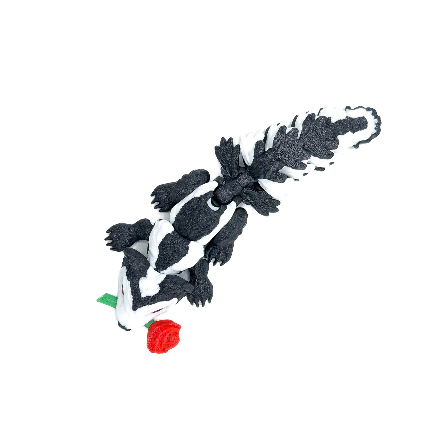 Top-down view of a black-and-white skunk figure with a red rose in its mouth, showing textured details on its tail, displayed on a white background.