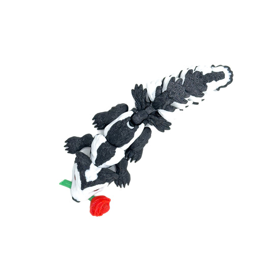 Top-down view of a black-and-white skunk figure with a red rose in its mouth, showing textured details on its tail, displayed on a white background.