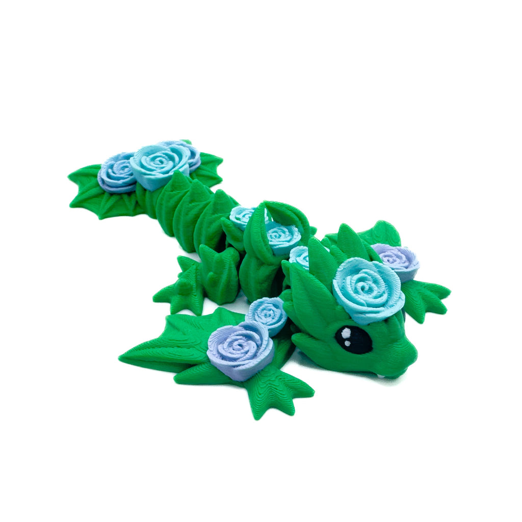 A green wyvern adorned with blue and light purple roses along its body, lying on a white surface with leafy details.